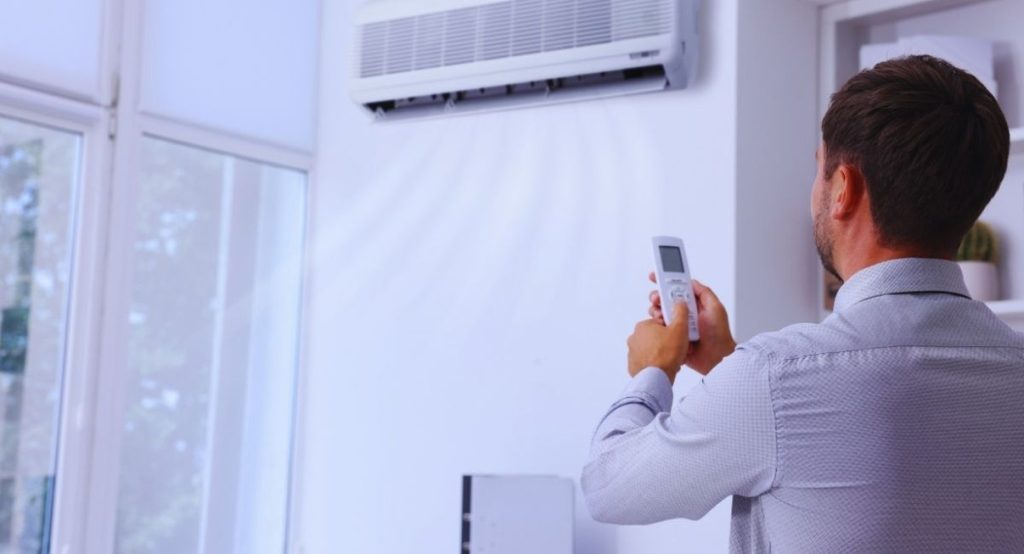 homme avec télécommande devant climatiseur mural - calcul puissance