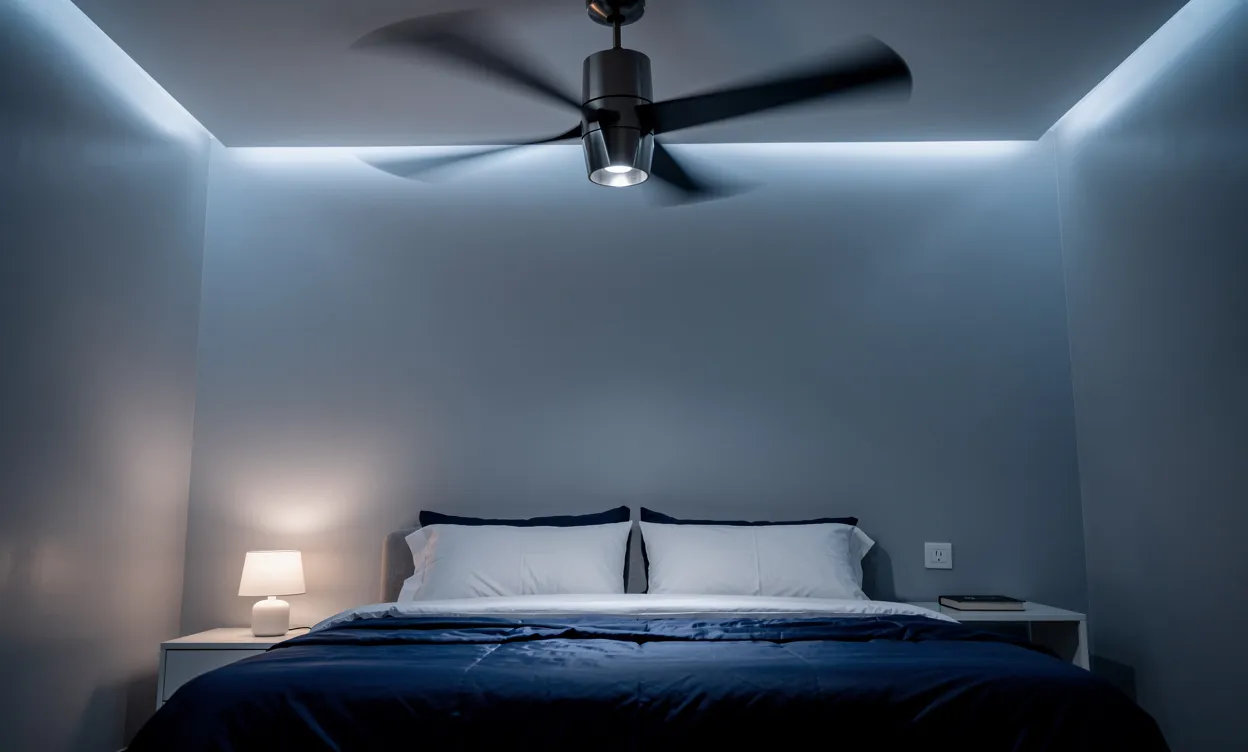 Un ventilateur de plafond moderne tourne doucement au-dessus d’un lit soigneusement fait dans une chambre paisible aux tons bleu nuit.