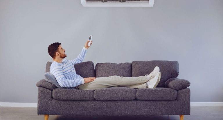 Homme allongé sur un canapé qui règle la climatisation avec une télécommande