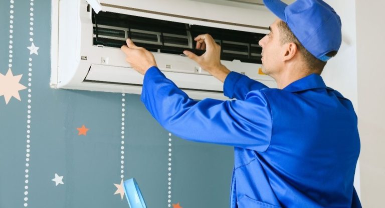 Technicien en combinaison ouvrant le filtre d'un climatiseur mural pour son entretien