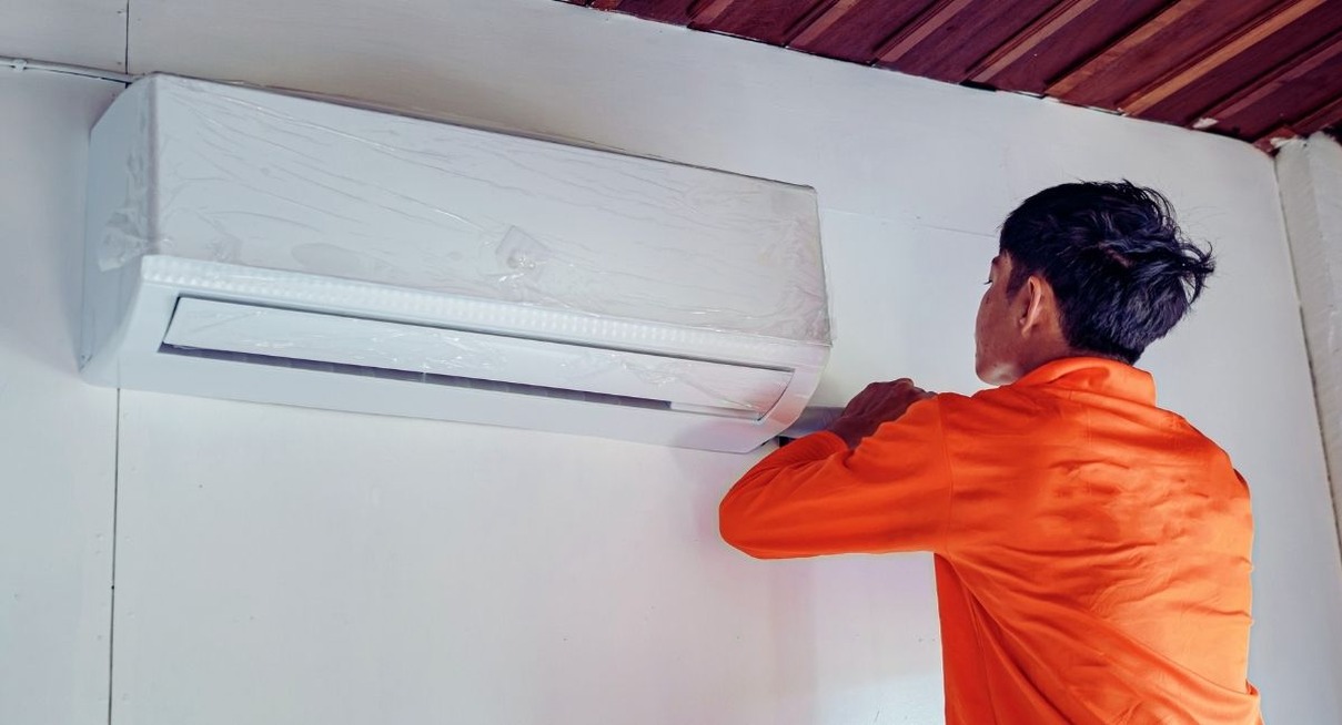 Technicien fixant une unité murale de climatisation encore sous film protecteur