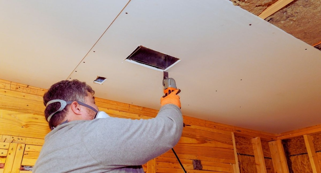 Ouvrier découpant le plafond pour poser une bouche de ventilation