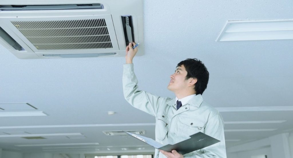 Technicien inspectant un climatiseur de plafond avec un devis en main
