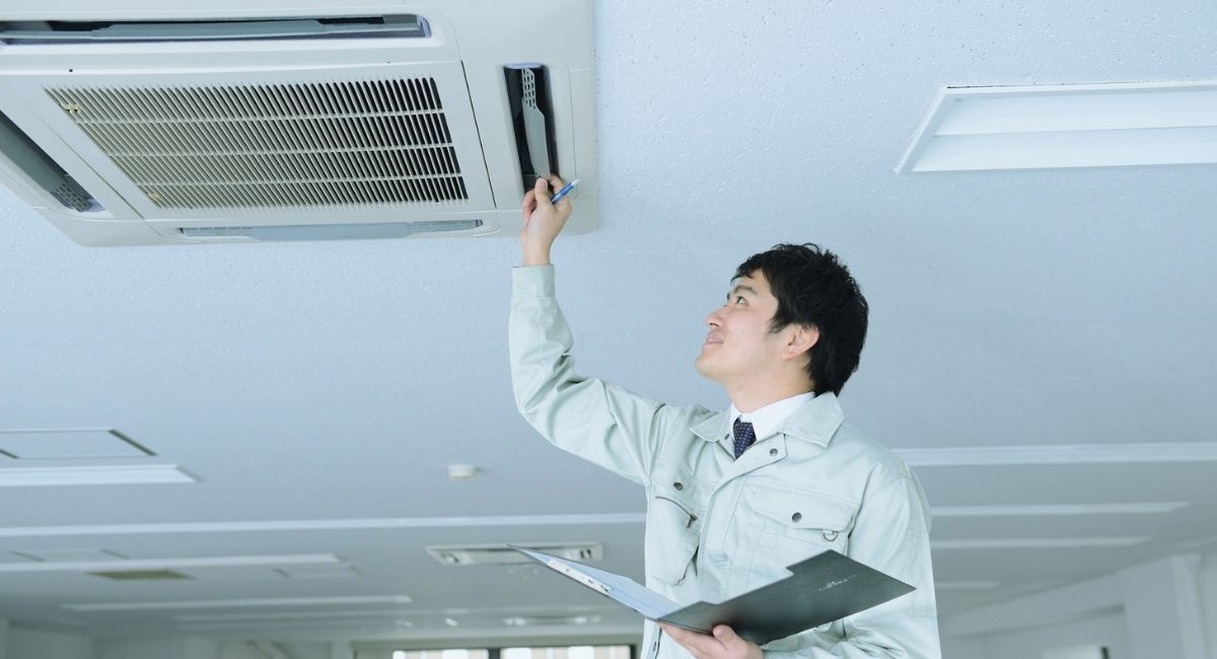 Technicien inspectant un climatiseur de plafond avec un devis en main