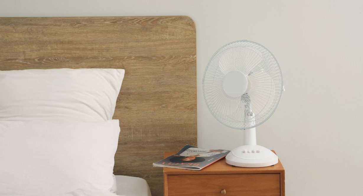 Ventilateur de table blanc posé sur une table de chevet en bois